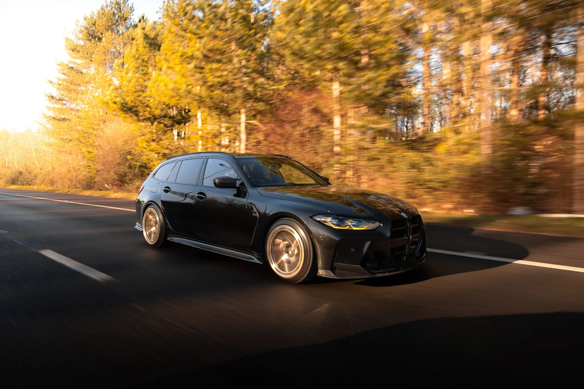 Black BMW G81 M3 Touring on gold Aphero AF-3 wheels driving through autumn light